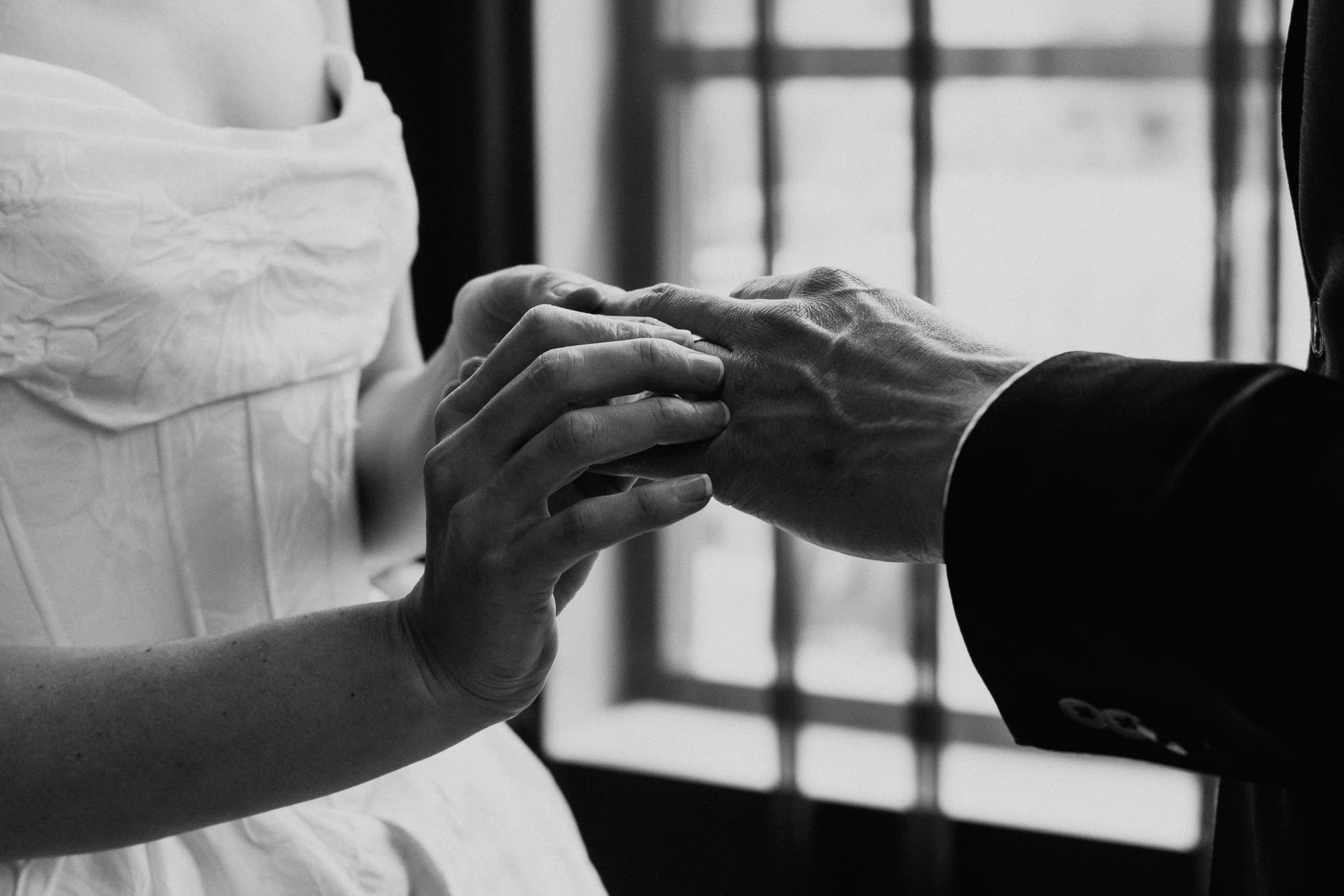 Black and white photograph of a ring being placed on the bride's finger